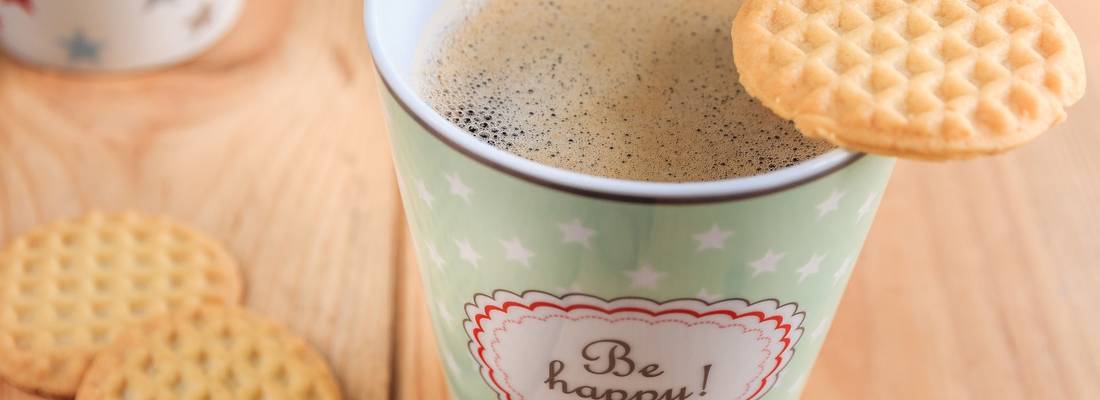Kaffeebecher mit dem Aufdruck "be happy" und Keksen