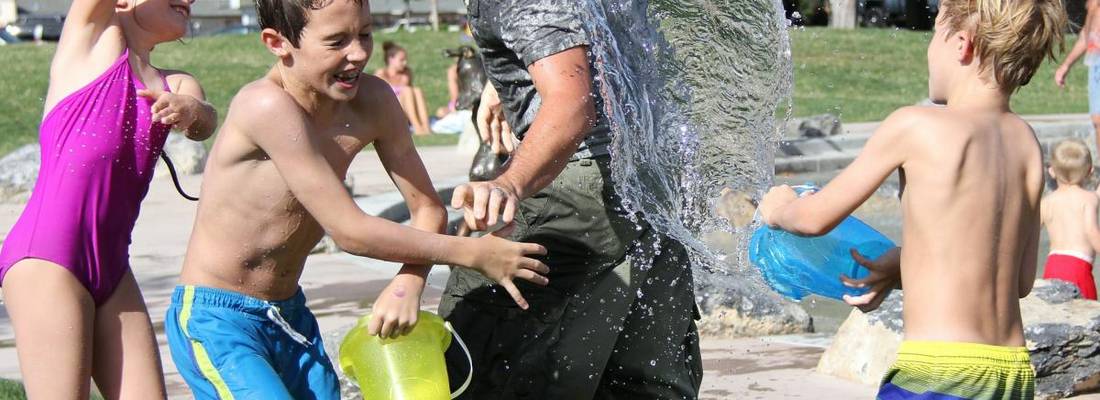 Drei Kinder bewerfen einen Mann mit Wasser. Alle lachen.