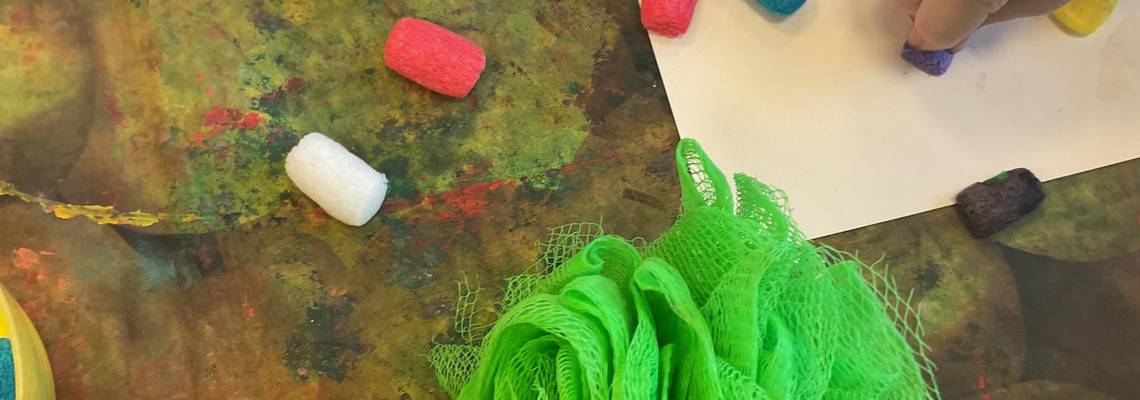 Ein KInd drückt ein farbiges Styroporstück auf ein Blatt Papier.