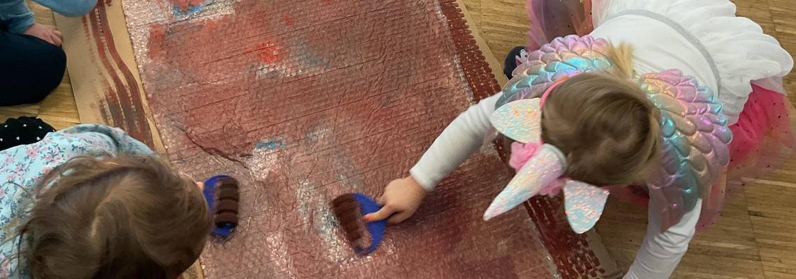 Drei Kinder bemalen mit einer Walze eine Folie.