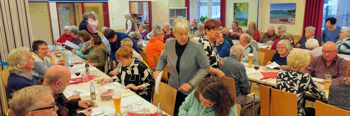 Männer und Frauen sitzen an langen Tischen in einem Raum.