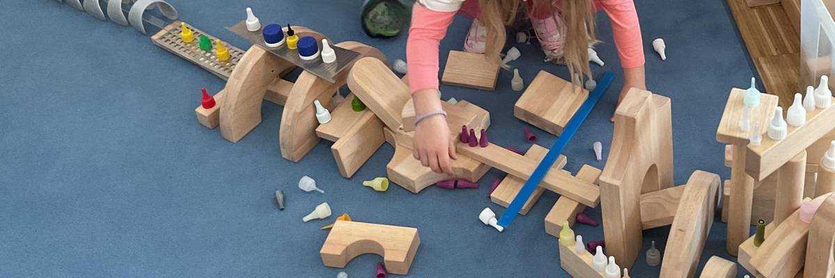 Ein Mädchen baut mit verschiedenen Materialien auf dem Bauplatz. Sie ist von oben fotografiert worden.