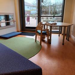 Ein Raum mit Möbeln und Matten auf dem Boden. Im Hinetrgrund blickt man durch ein Fenster.