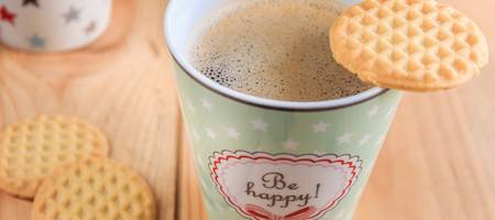 Kaffeebecher mit dem Aufdruck "be happy" und Keksen