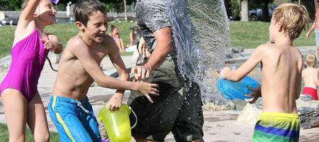 Drei Kinder bewerfen einen Mann mit Wasser. Alle lachen.