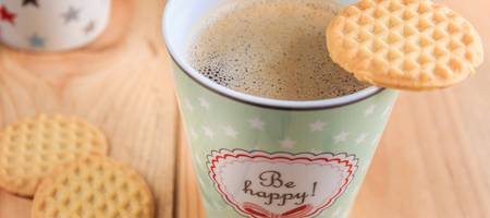 Kaffeebecher mit dem Aufdruck "be happy" und Keksen